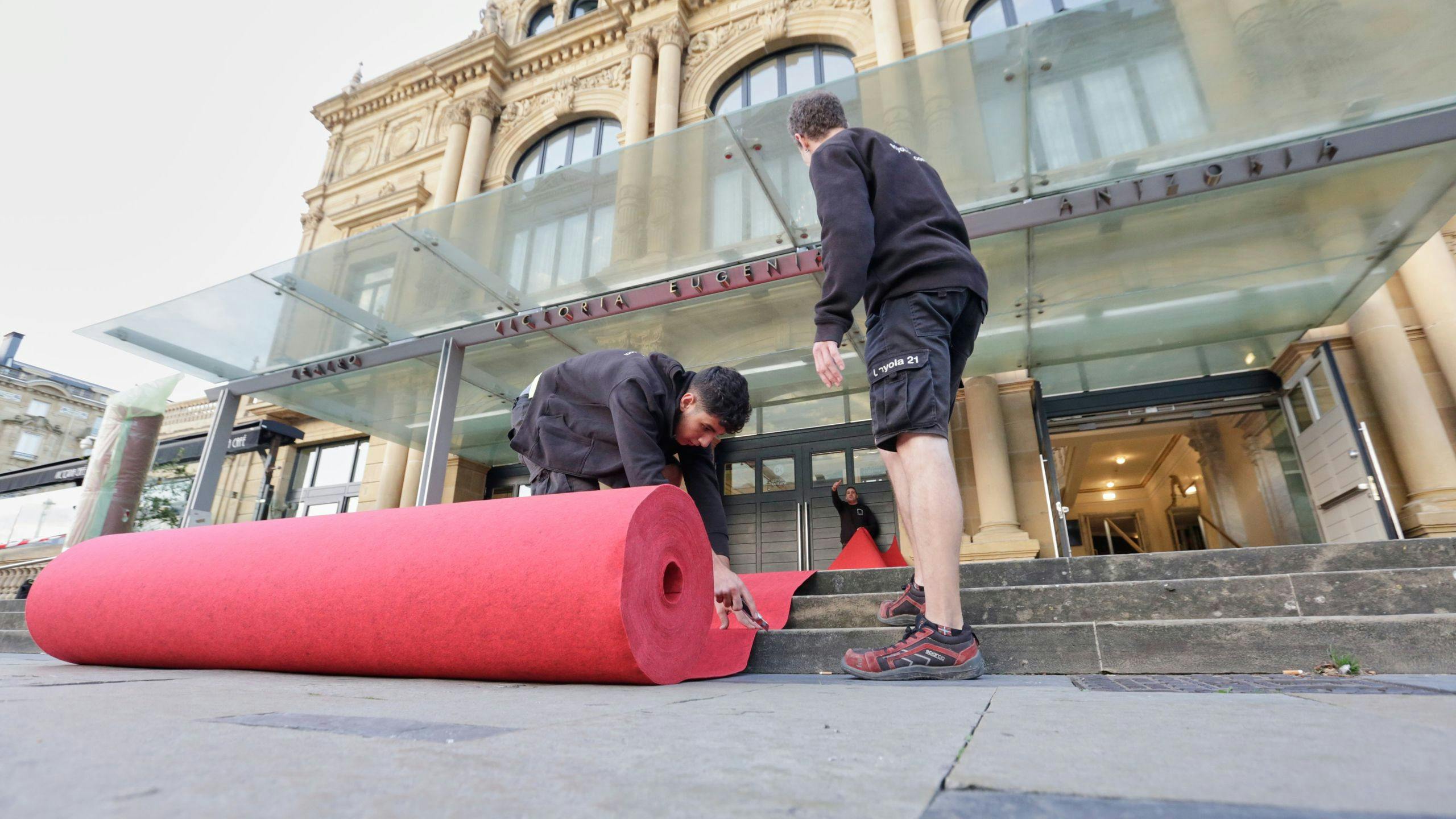 Dos operarios del Festival de San Sebastián despliegan la alfombra roja ante el Teatro Victoria Eugenia