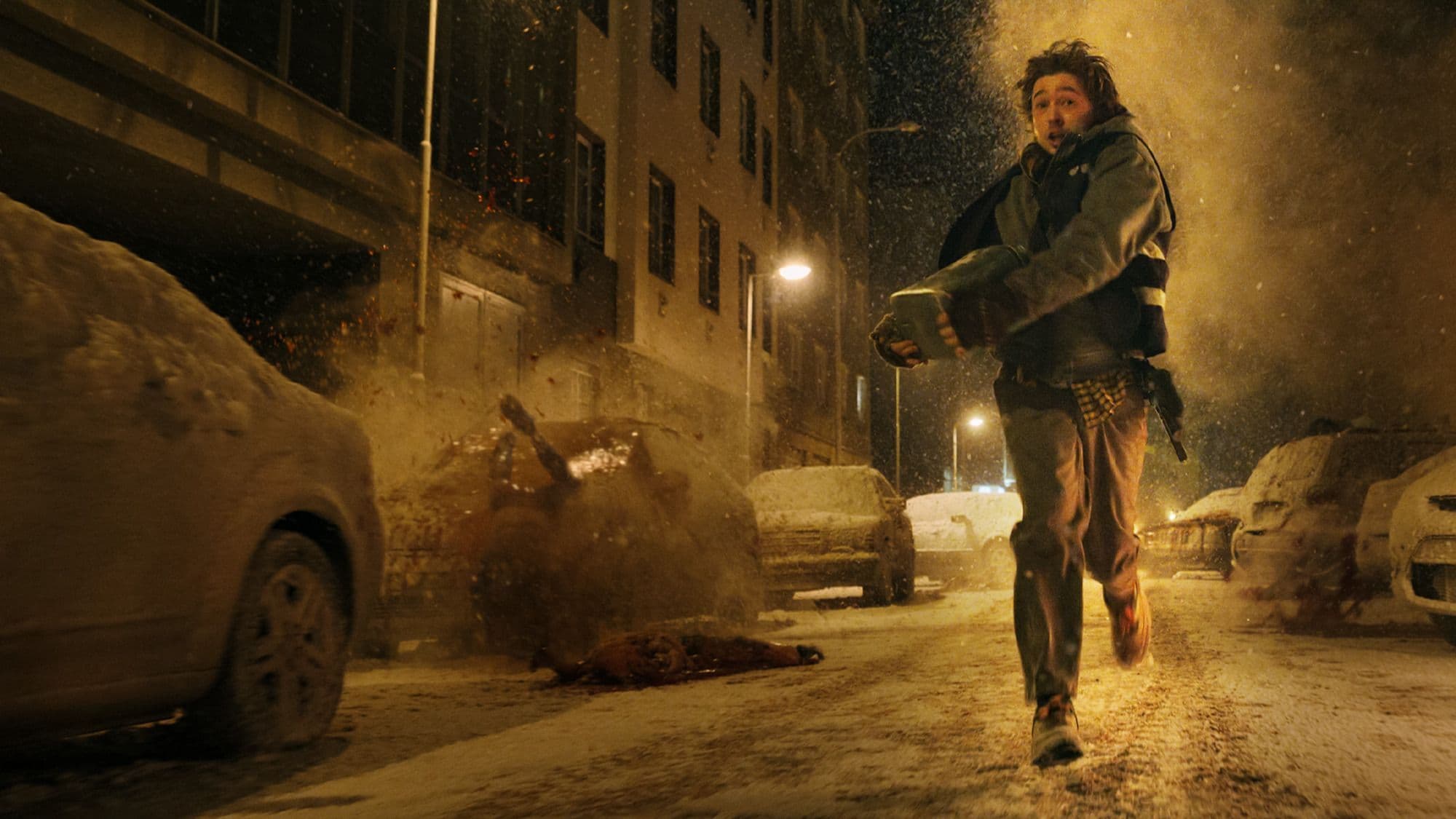 Austin Abrams corre por una calle nevada mientras caen cadáveres a su alrededor en una escena de 'Resident Evil' (2026)